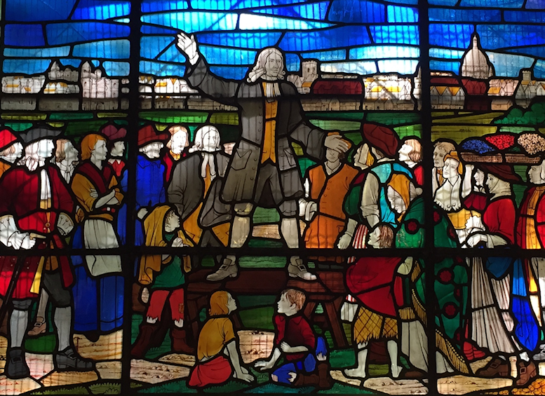 Stained glass representation of John Wesley standing on a bench while preaching outdoors to a crowd of people